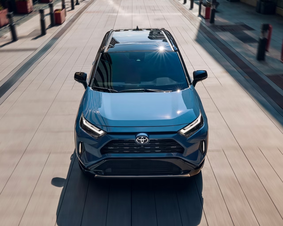Front view of the blue Toyota RAV4 hybrid parked in bright light in a modern driveway, showcasing the bold design of the grille.
