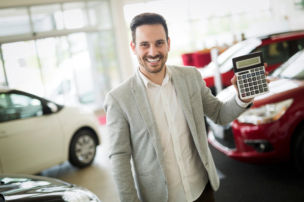 Un vendeur de voiture dans son garage qui tient une calculatrice dans sa main.