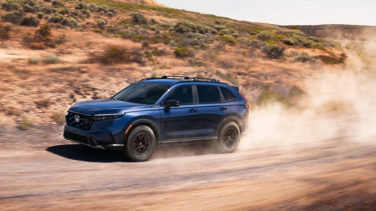 Honda CR-V hybrid 2026 dark blue driving on a deserted dirt road, raising dust, showcasing its off-road abilities.