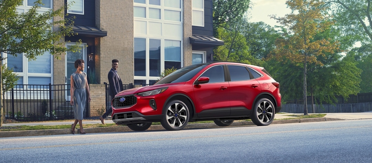 Couple looking at a parked red Ford Escape hybrid in front of an urban house, symbolizing local accessibility for test drives.